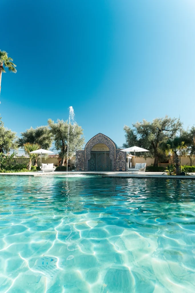 Piscine extérieure aux eaux turquoise avec fontaine et arche en zelliges – villa de luxe Amanaya Marrakech